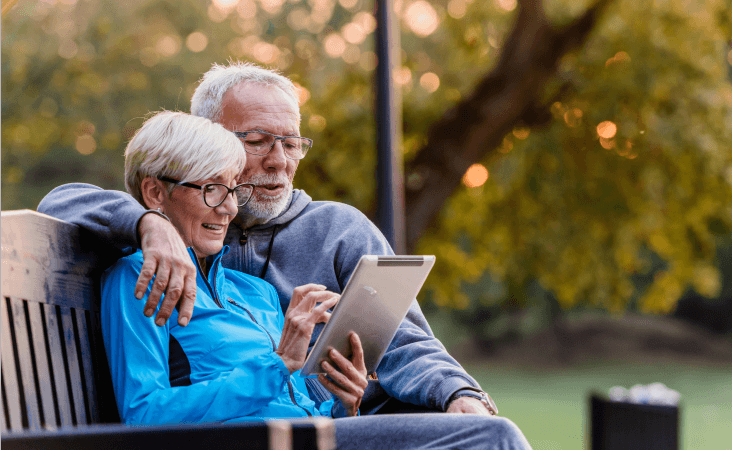 Older couple sitting together on bench scrolling on tablet
