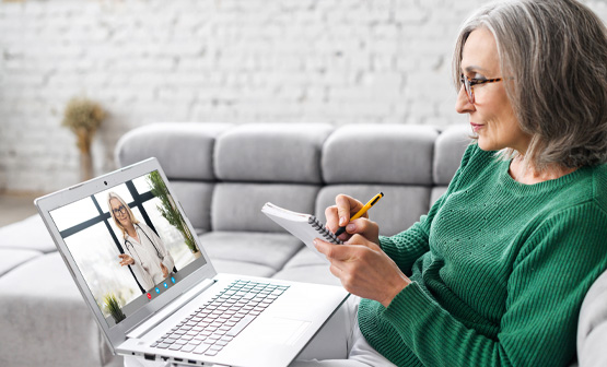 Una mujer mayor escribe en un cuaderno durante una videoconferencia con un médico